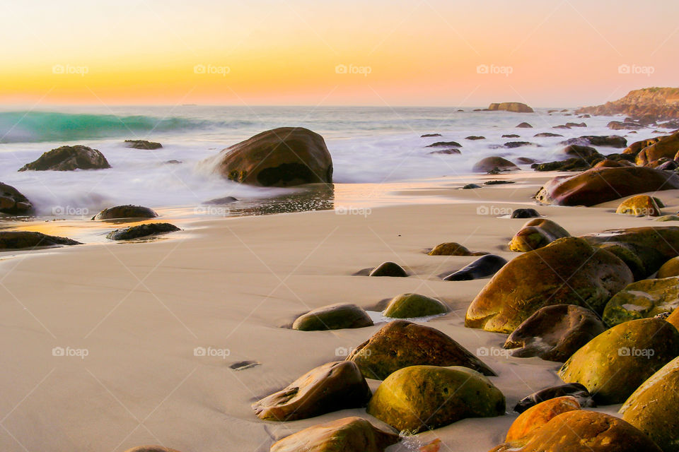Sunset over boulder beach. Golden hour with the sea and beach and large rocks.
