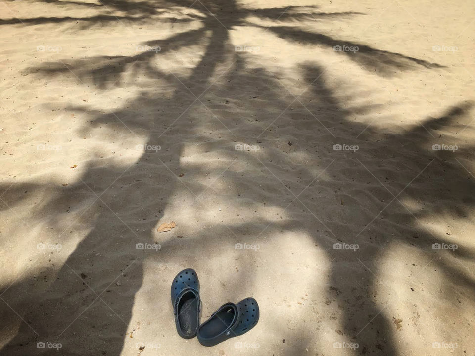 Palm tree shadows and a pair of Crocs on sand beach