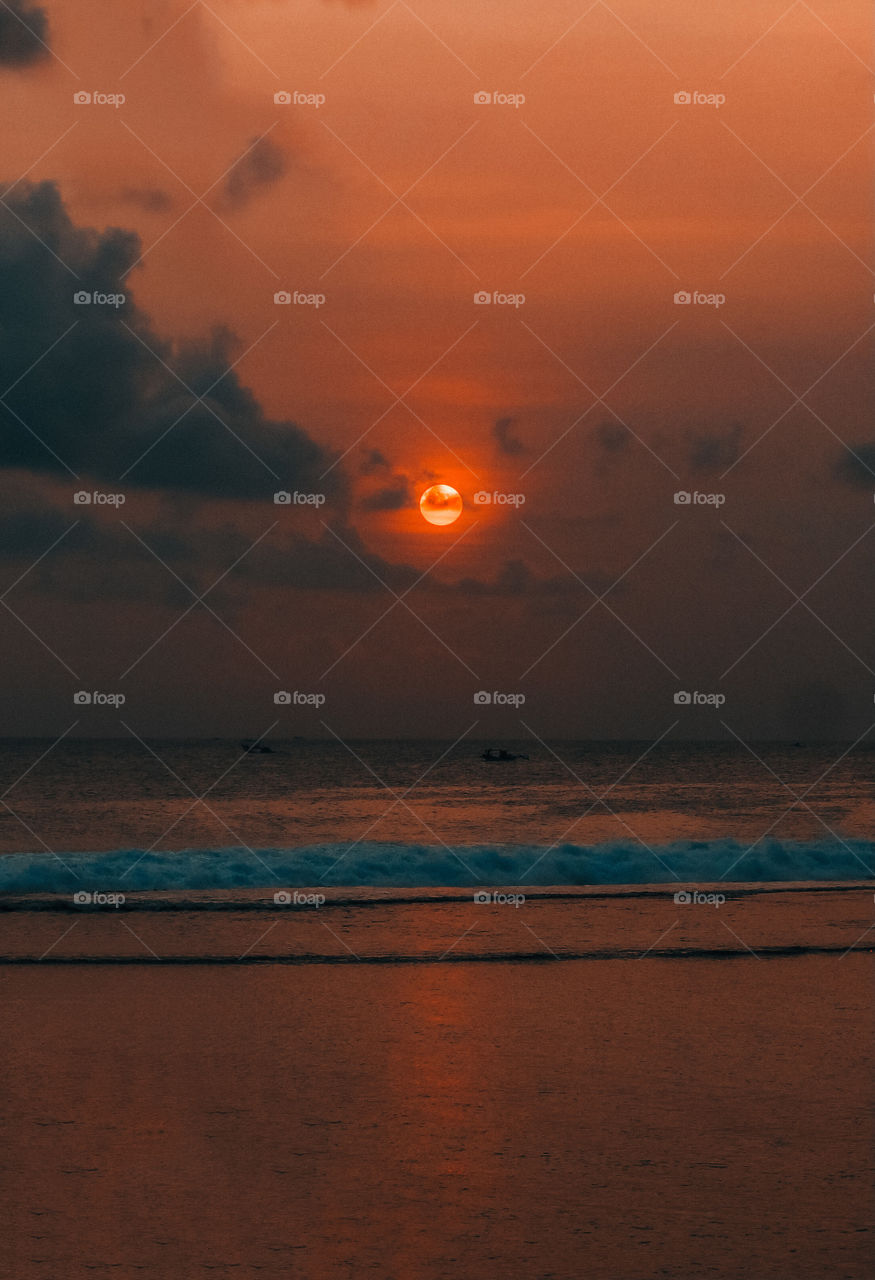 the moment when the sun goes down with a view of the beach and the waves are calming and there are 2 fishing boats 