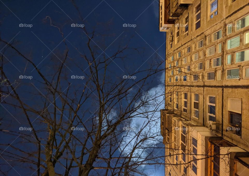 night sky with clouds and stars against the background of a tree and a residential building