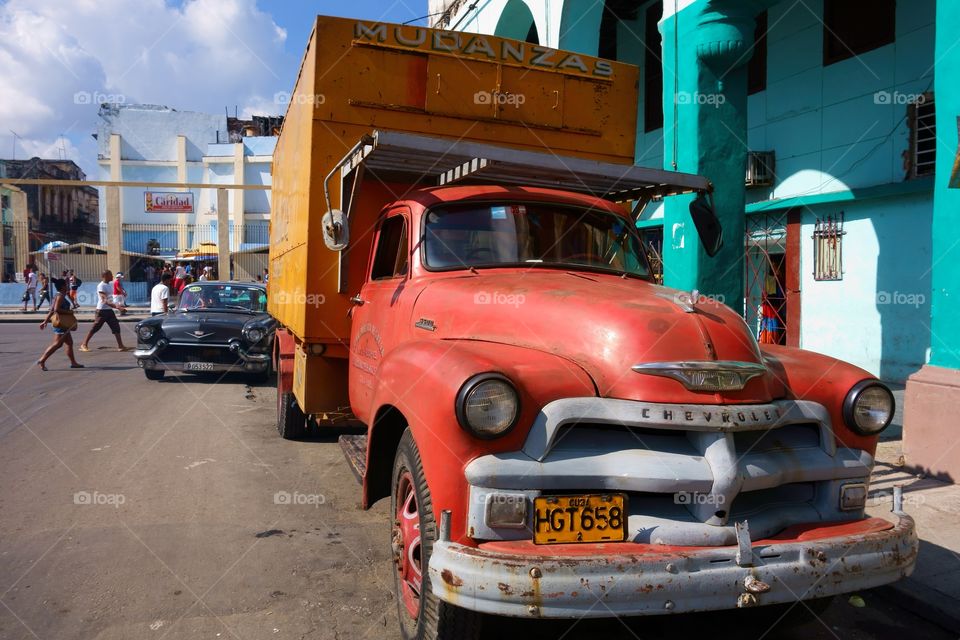 Havana, Cuba - December 26, 2013: Old American truck and a busy street with pedestrians, truck parked in front of colorful building representing classical architecture of Havana, Cuba on December 26, 2013.
