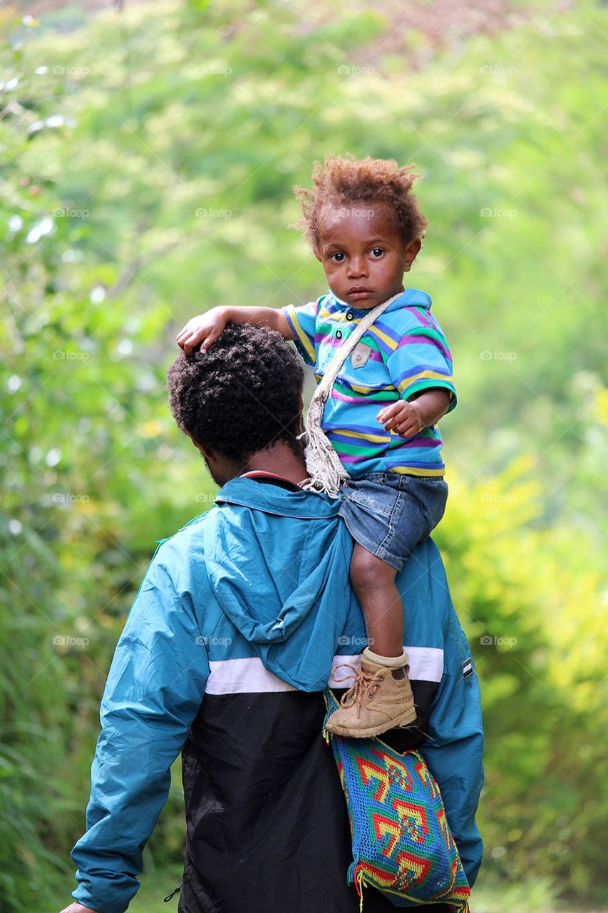 son having a ride home on his father's shoulder. Hakwange village, Menyamya, Papua New Guinea