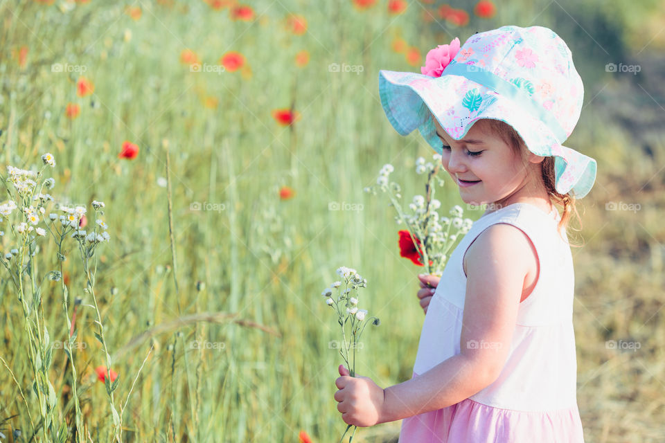 Lovely little girl in the field of wild flowers. Cute girl picking the spring flowers for her mom for Mother's Day in the meadow. Girl holding bouquet of flowers. Spending time close to nature