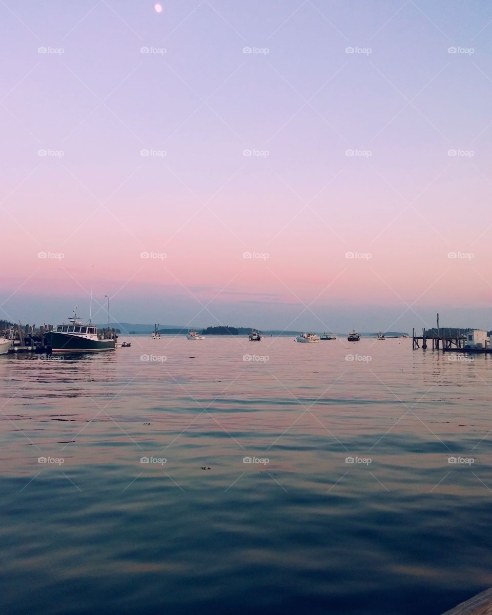 pink and purple sunset over ocean with boats in background. set in maine