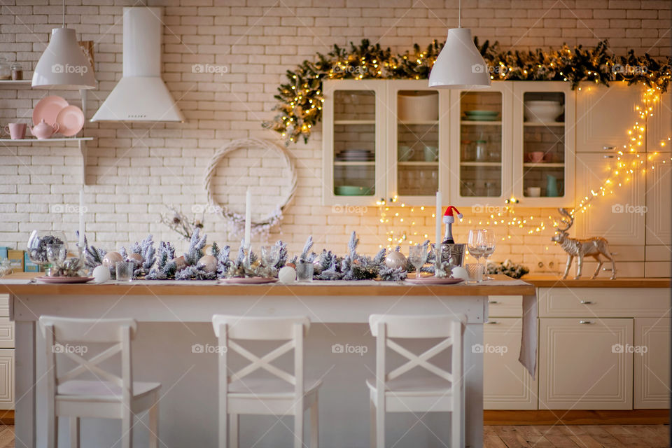 Festive winter cozy kitchen interior with garlands, decorations and gifts.  Christmas dinner at the decorated table.