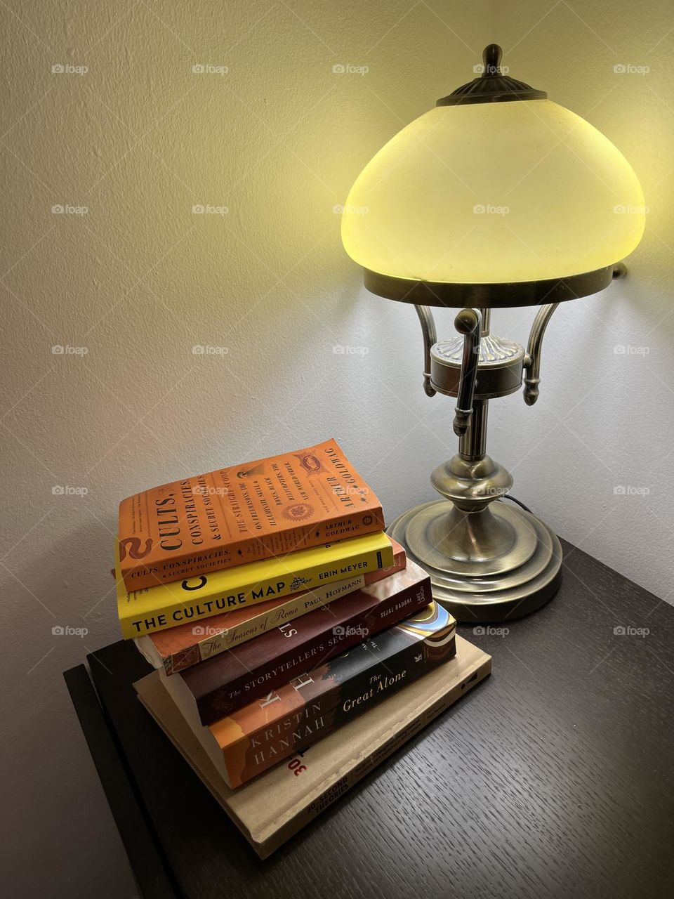 Books by the nightstand with a yellow light.