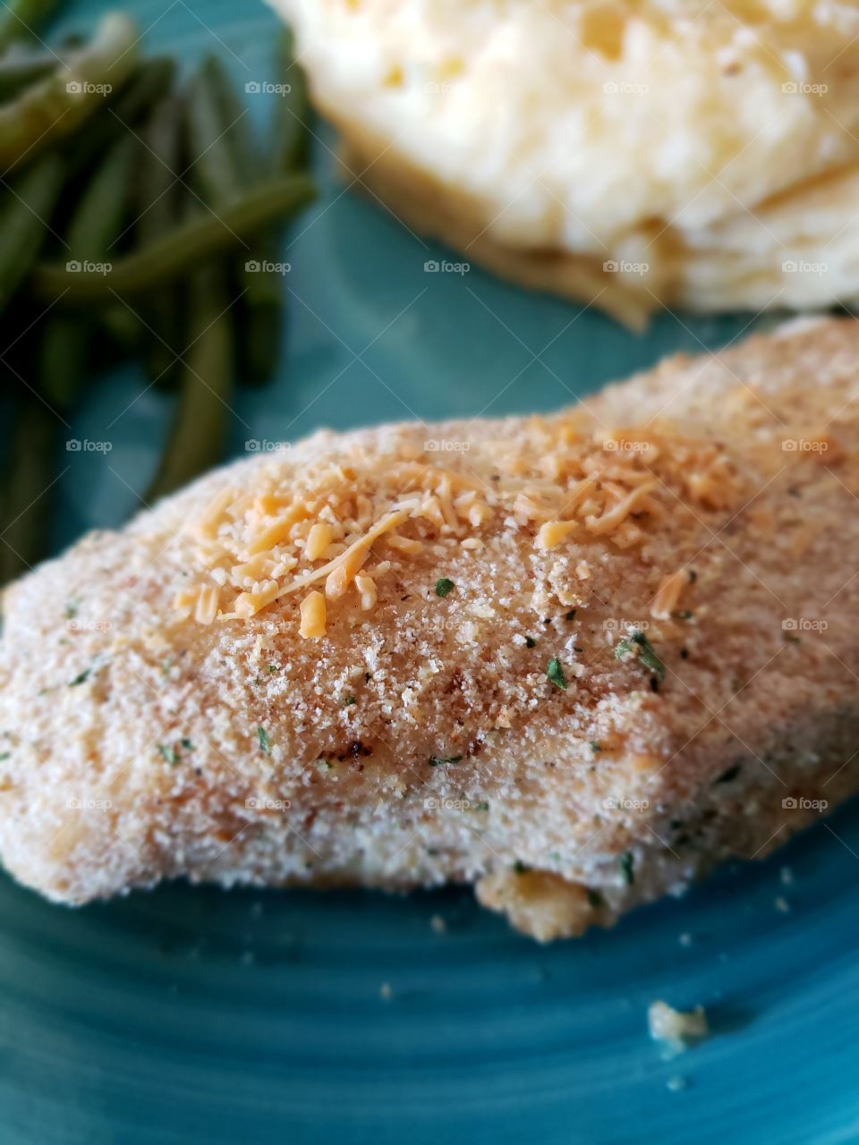 Fine details on a freshly baked chicken breast on a plate served with mashed potatoes and green beans.