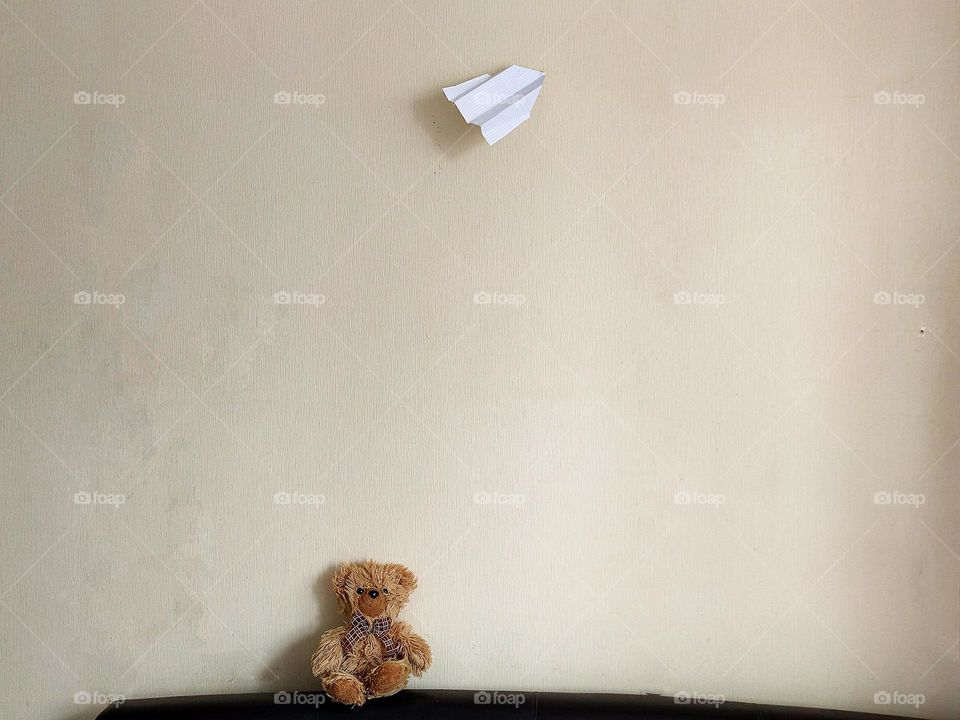 Minimalism of objects in space.  Teddy bear and white paper airplane on the background of a beige wall.  Contrast of objects.