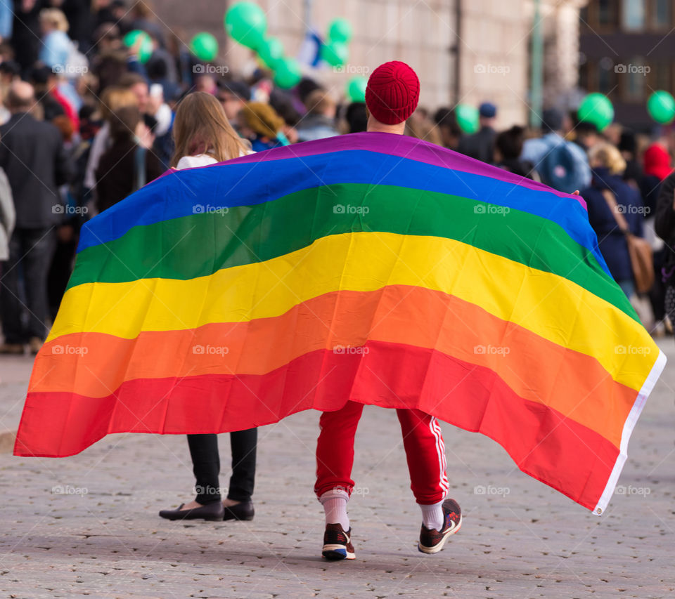 Helsinki, Finland – September 24, 2016: Unidentified protester march with large gay / LGBT rights rainbow flag on his shoulders on the cobble street in front of the Helsinki Cathedral on Senate Square in a demonstration against racism and right wing extremist violence in the very center of Helsinki, Finland on 24 September 2016.