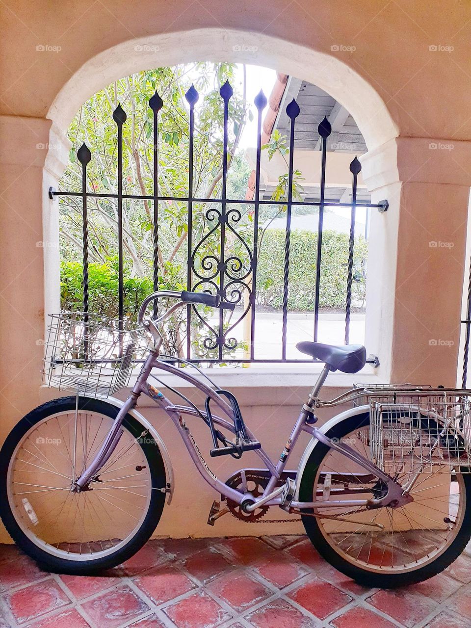 A lilac colored bicycle sits propped up against a window in an entryway of an office building.