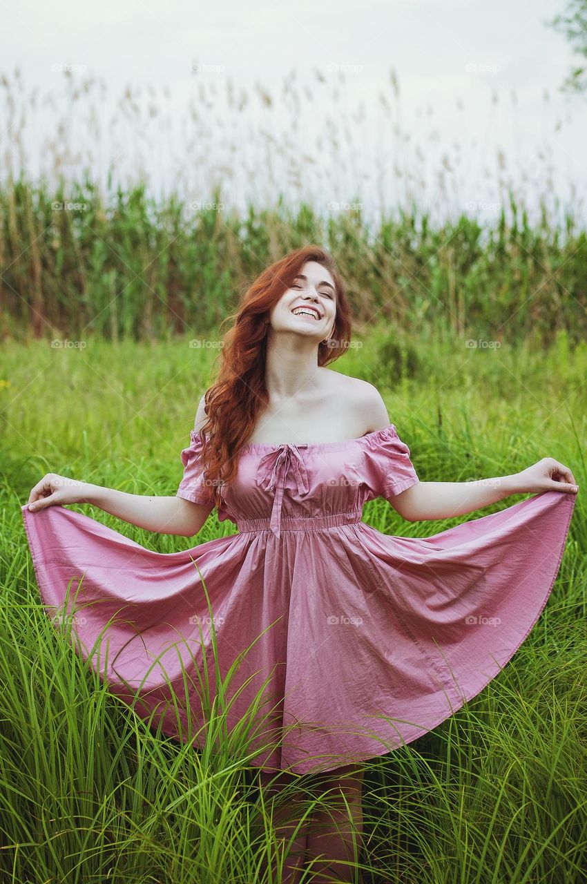 Portrait of beautiful young redhead woman, girl in pink dress sitting  outdoor, in the summer park, meadow with green grass