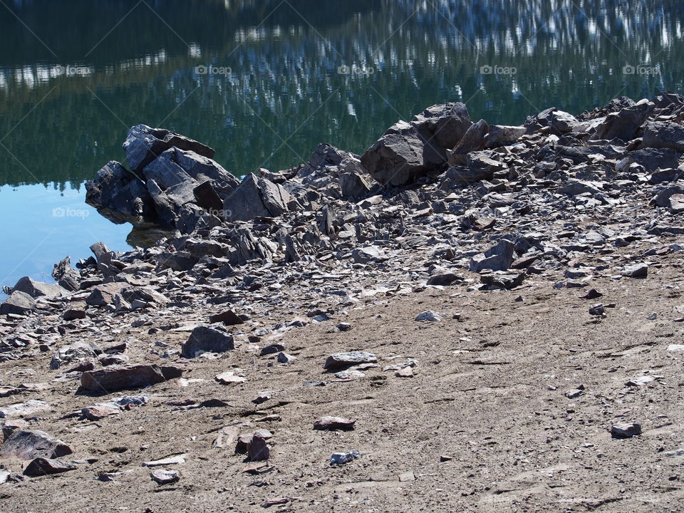 Jagged rocks and boulders along the shoreline of Ochoco Lake in Central Oregon on a sunny spring day.