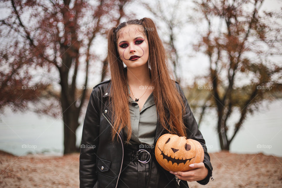 Young Woman holds a pumpkin in her hands. Painted pumpkin. Woman with bright makeup for Halloween. Halloween 2020. Place for inscription.