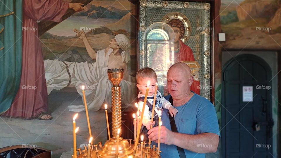 father and son put candles in the temple