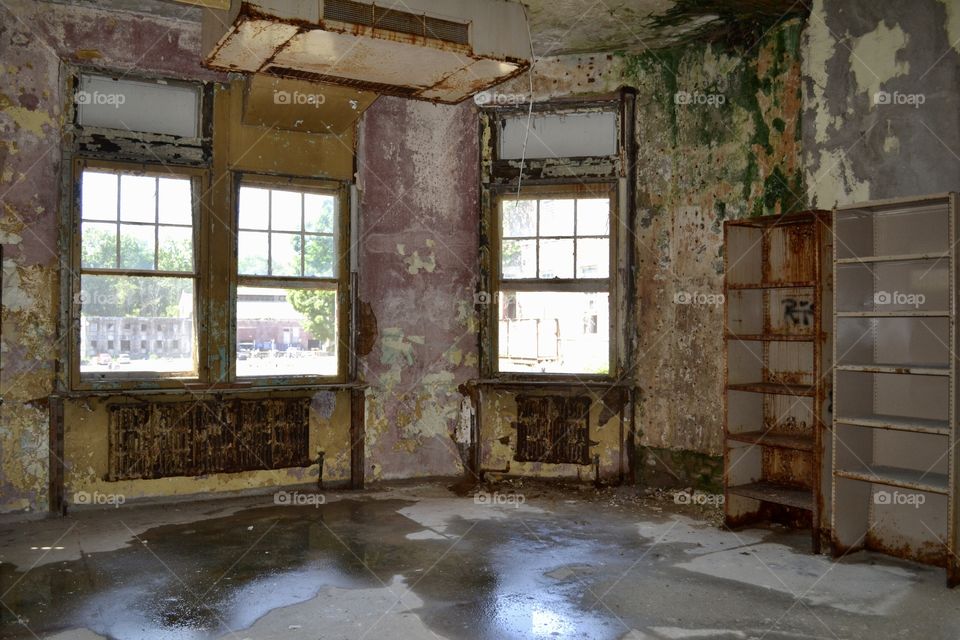 A room inside of an abandoned building with pealing paint and wet floors and broken windows