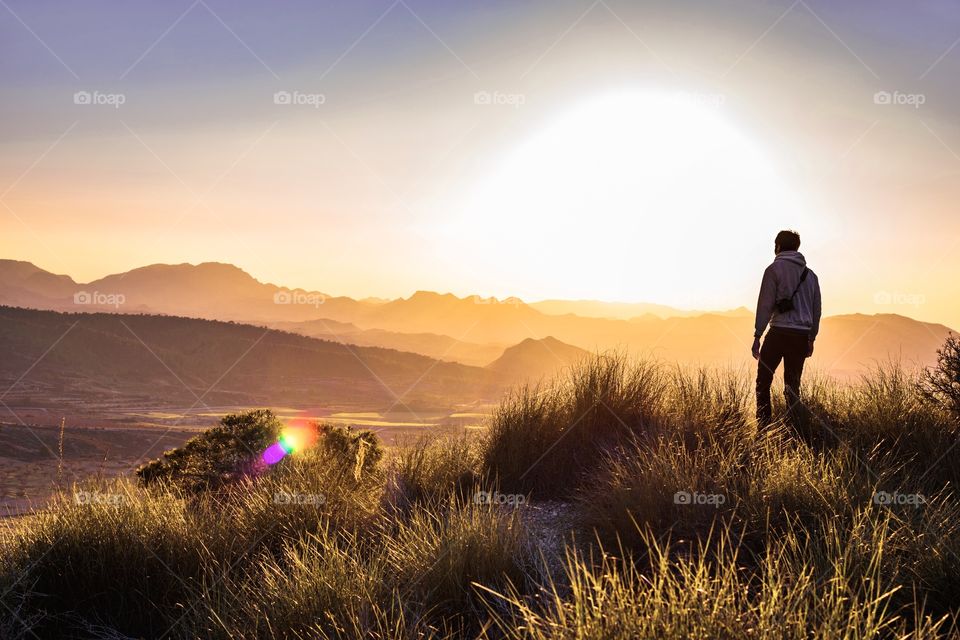 Man standing at a mountaintop against foggy landscape at sunset