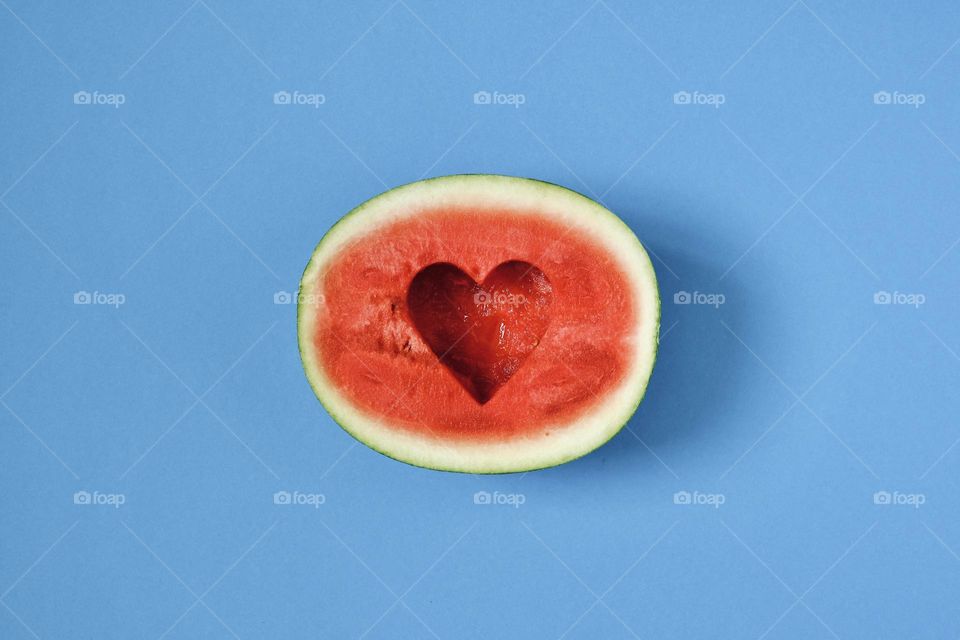 Directly above view of a half of a watermelon with a heart shaped cutout isolated on blue background. 