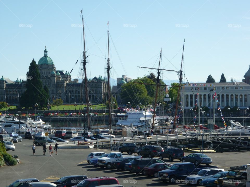 As masts from an older sailboat tower in the harbour, the Parliament buildings and Museum stand in the background in Victoria, British Columbia 
