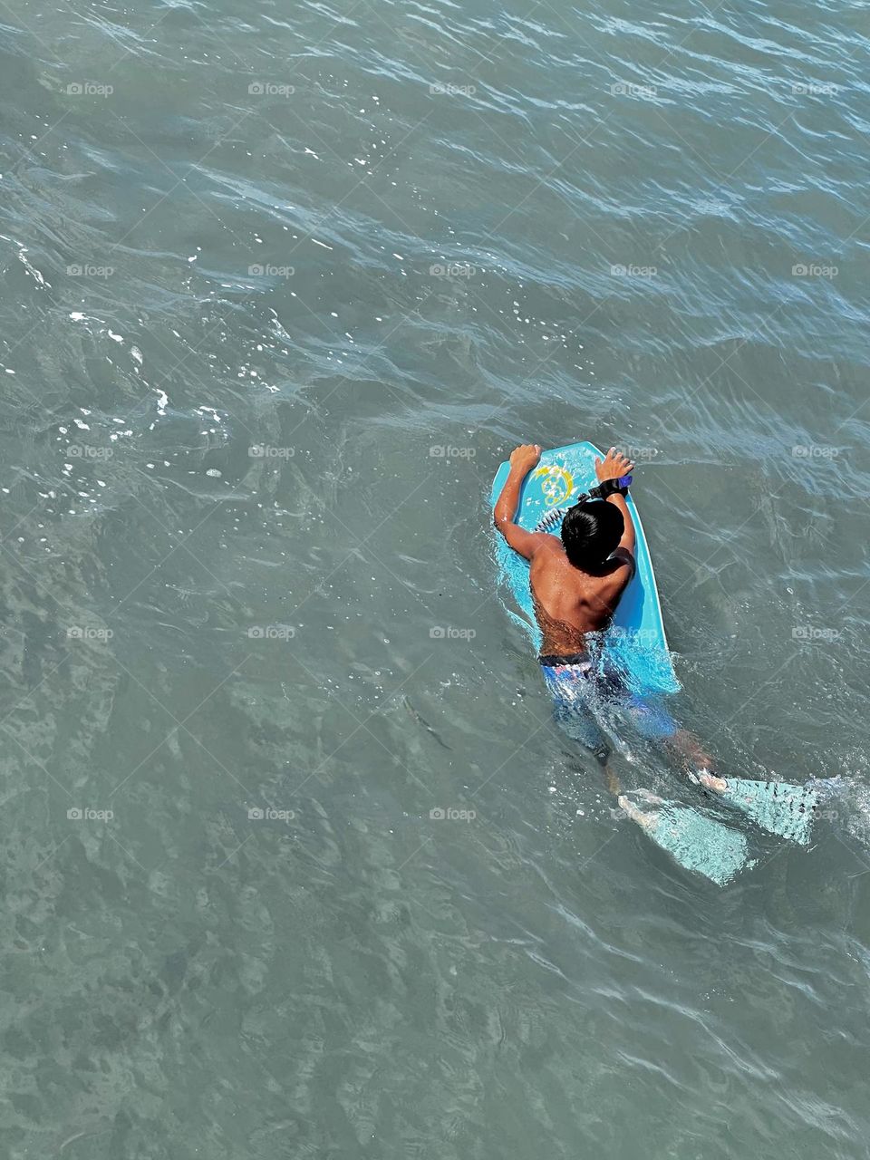 A young boy with aqua fins on a boogie board looking for his next wave