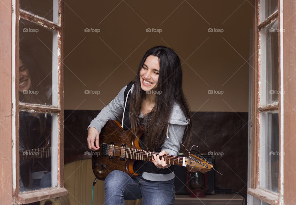 Beautiful woman guitarist playing a guitar and smiling on the window