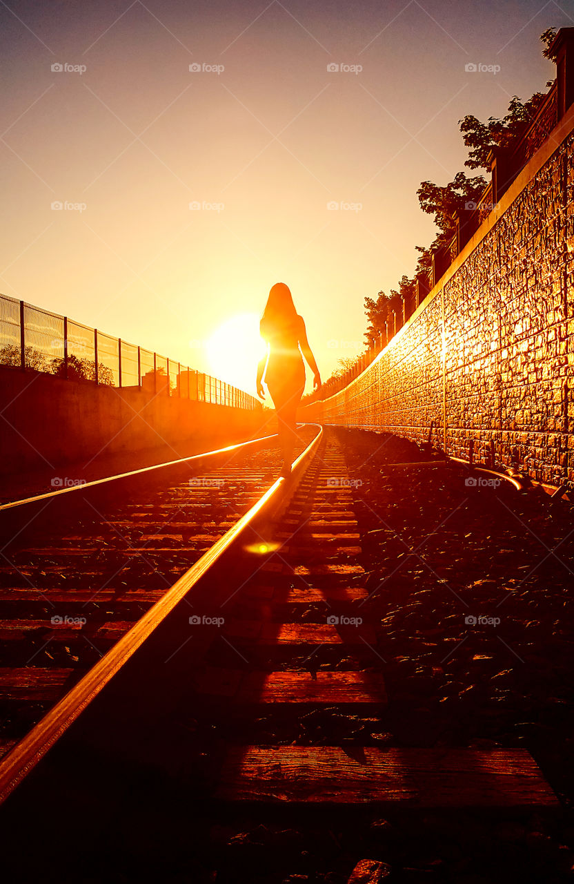 Woman is walking on a railway in the rays of a sunset