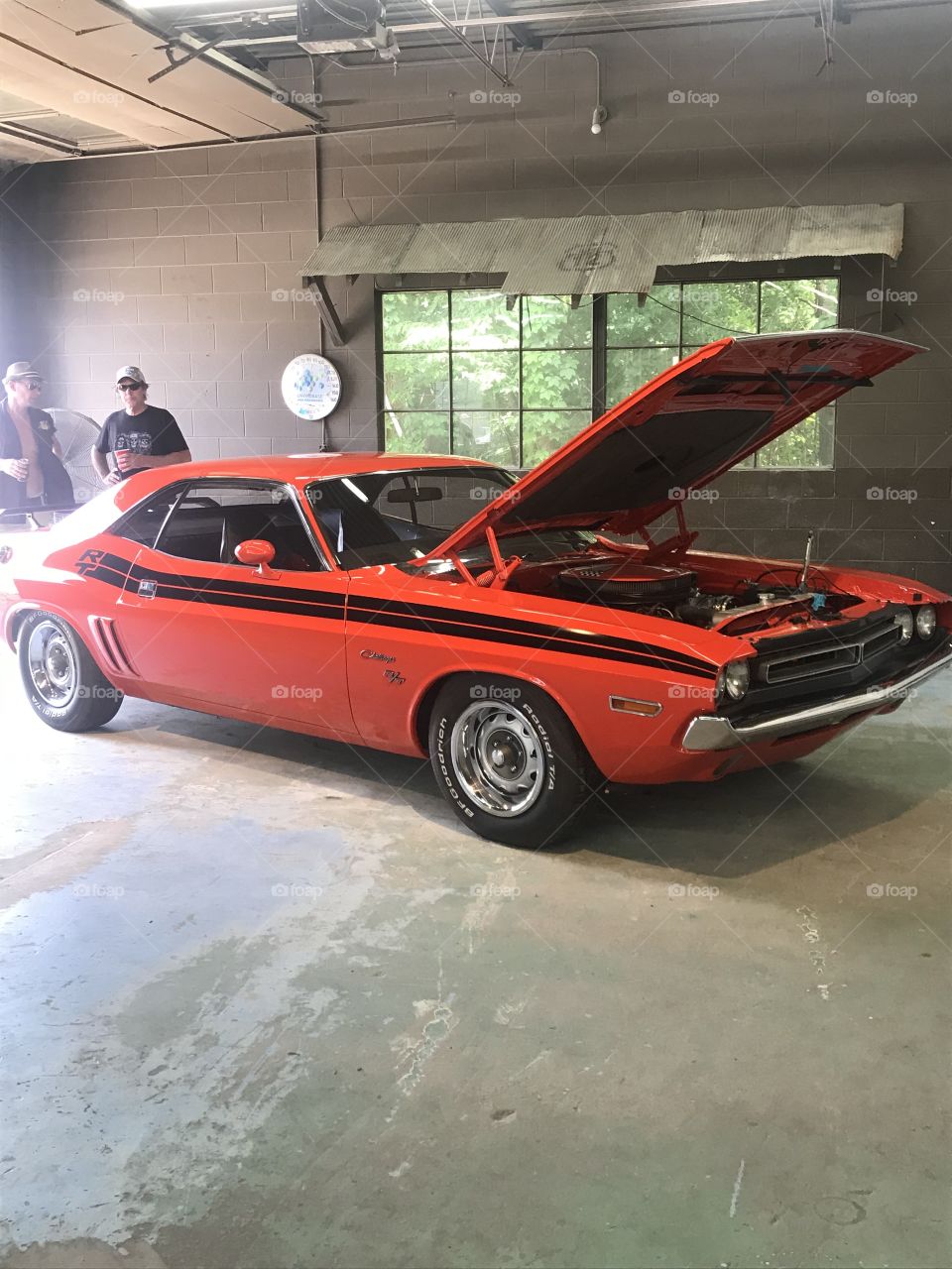 A red antique car with a black stripe and an open hood in a garage