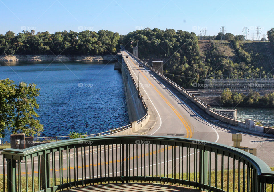 The view of a lake and the road across its dam from an observation deck high above. 