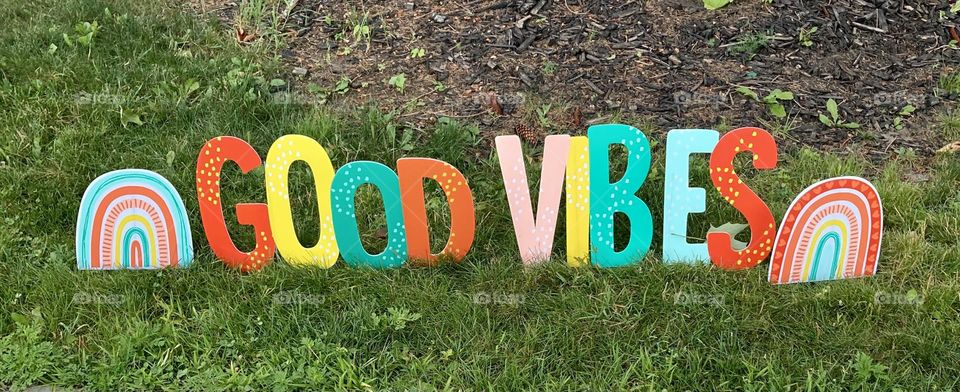 Rainbow coloured Good Vines sign on a lawn.