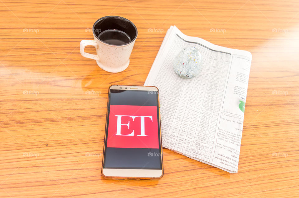 Kolkata, India, February 3, 2019: Economic Times (ET) news app visible on mobile phone screen beautifully placed over a wooden table with a newspaper and a cup of coffee. A Technology Product Shoot.