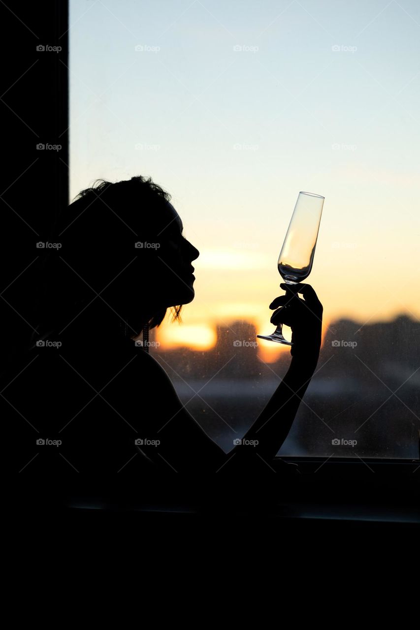 Silhouette of a beautiful woman with a glass by the window at sunset.