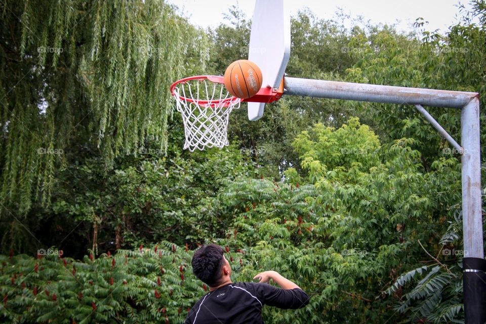 Teenager boy is taking a shot at a basketball court