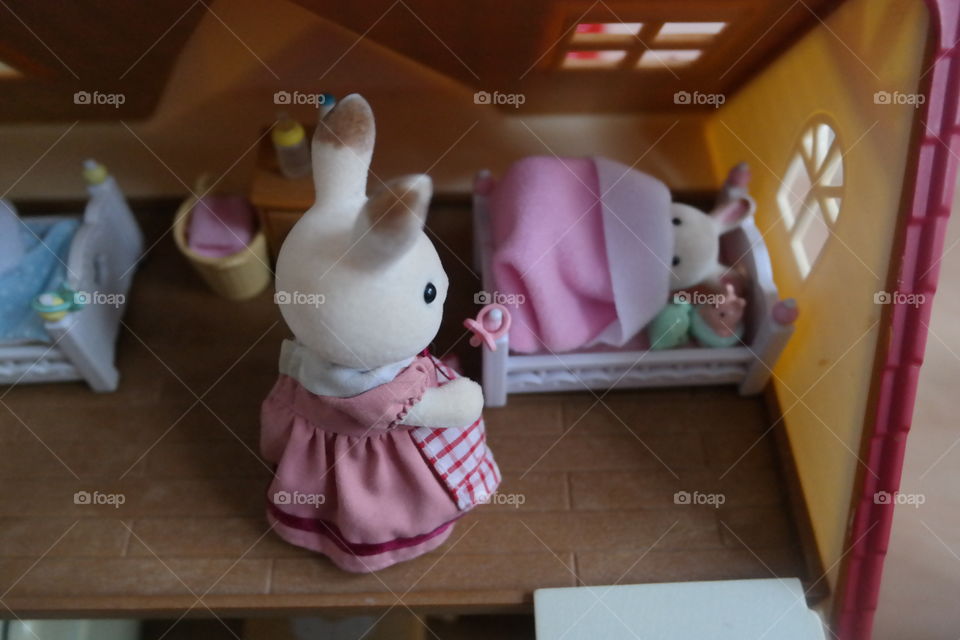 mama bunny tucks baby girl bunny into her crib with comfy plushies and a cozy pink quilt