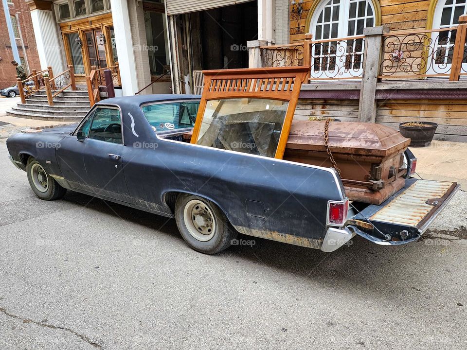 A 1970 Chevy El Camino is loaded down with a mirror and a casket creating an unusual freight load