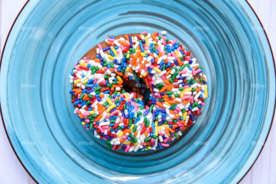 Close-up flat lay of a multicolored sprinkle donut on a blue plate