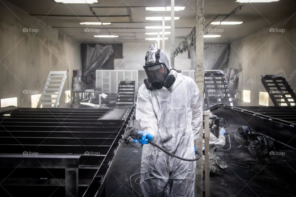 A hard working person paints in a factory paint suit.