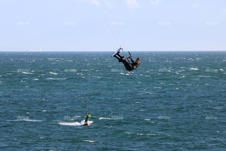 Kitesurfers, one jumping over , the other one riding with the wind ,against the blue ocean 