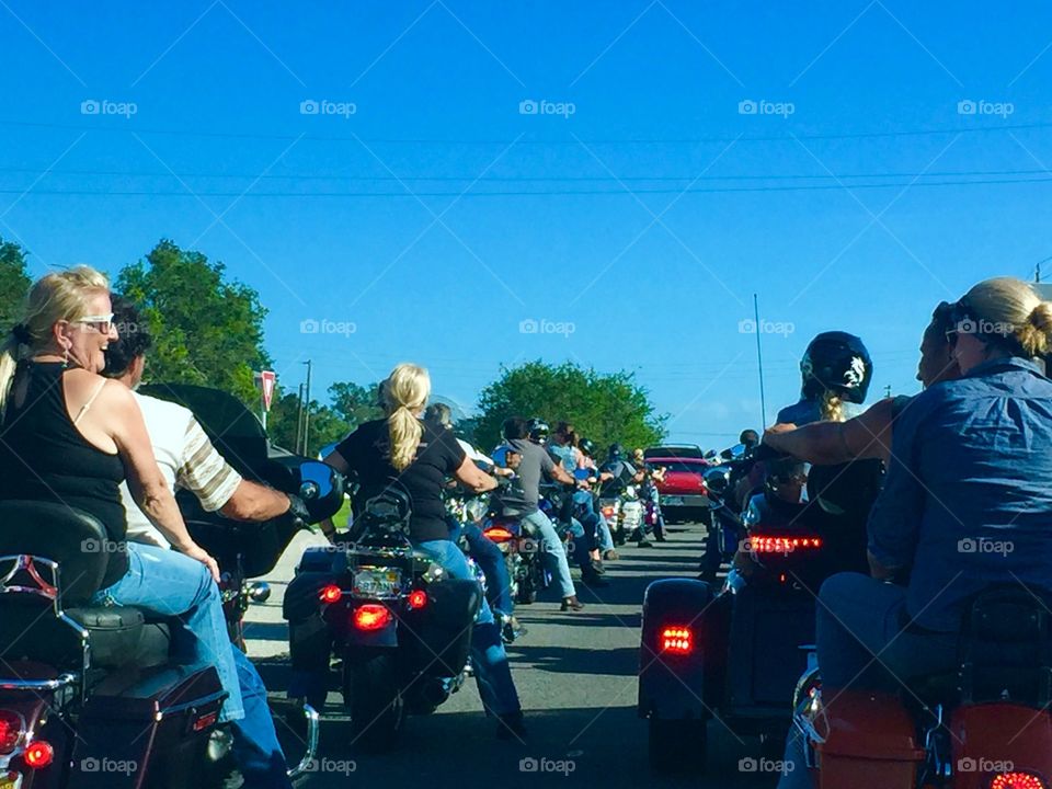 Motorcyclists in Daytona Beach and Ormond Beach Florida during Biketoberfest biker festival. Rear view with men and women riding Harley Davidson, Honda, BMW motorbikes, trikes and 3-wheelers. Bikers wait at light with line of cars, views from behind. 