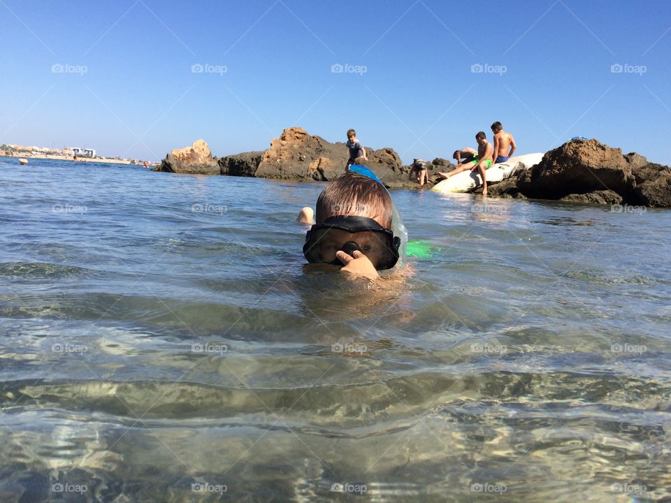 Boy diving with a mask in sea making a gesture with his fingers