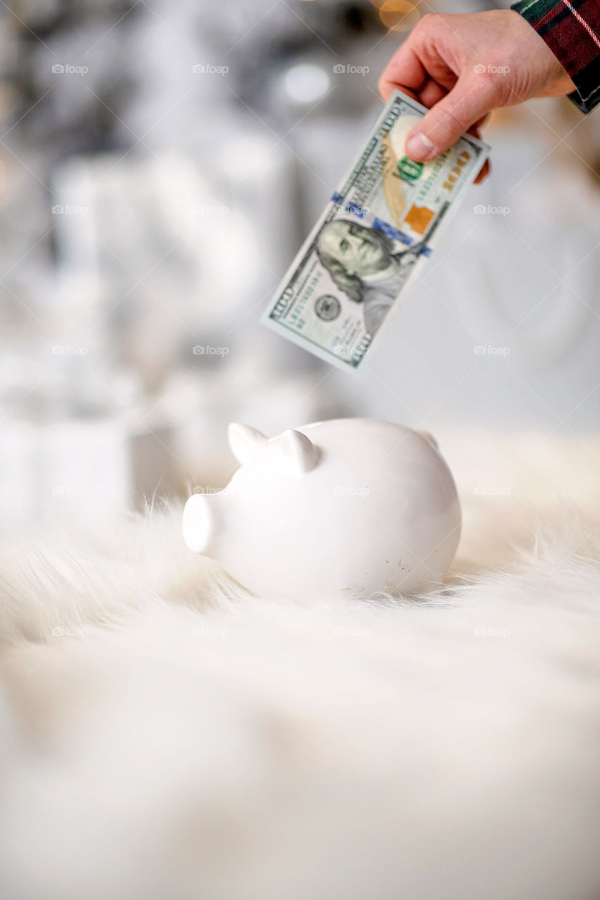 piggy bank with 100 dollars banknote in festive New Year atmosphere of scenery. Magical bokeh with Christmas tree and bright lights.