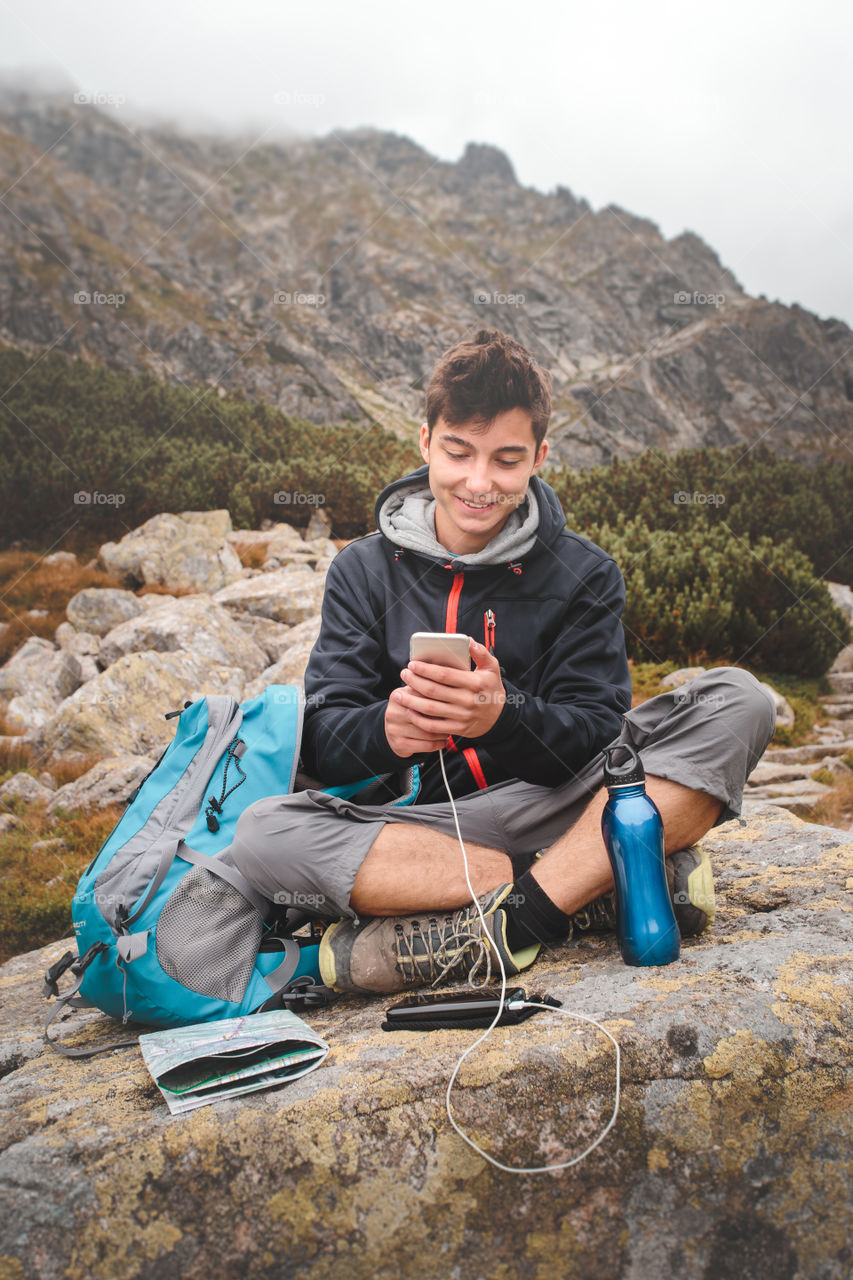 Teenage boy using smartphone and sitting on rock