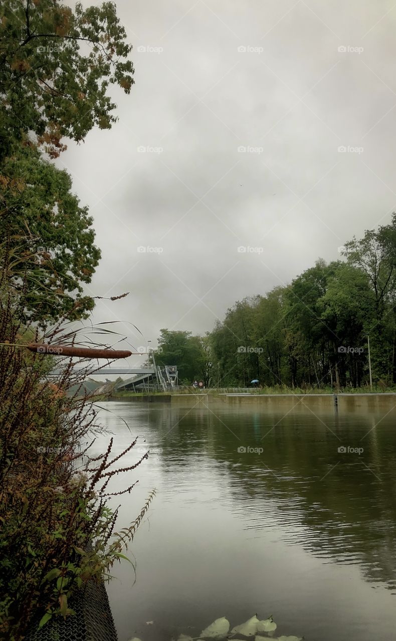 Grey rainy clouds on a fall day over the water of river running through the woods