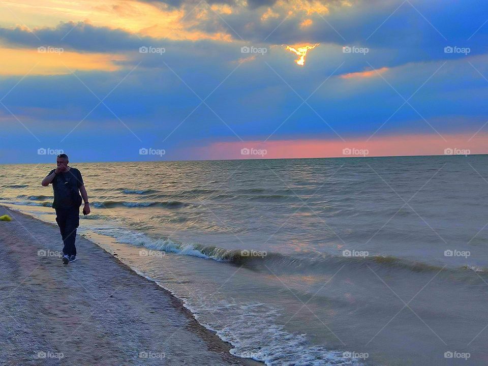 Sunset on the sea. The movement of the waves of the sea. The red stripe of sunset separates the stormy sea from the dark clouds of the sky. A man walks along the seashore