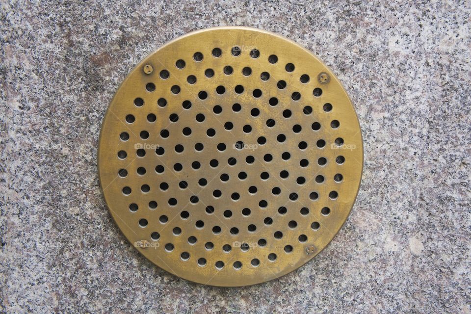 A circular brass vent on the exterior of a commercial building in New York City.