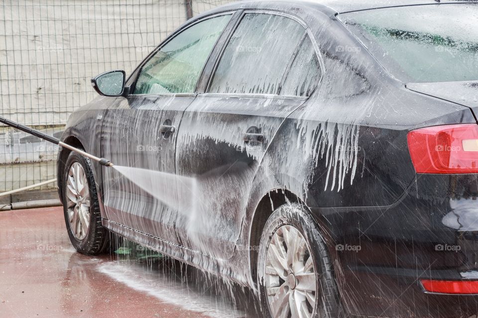 A black car with foam and bubbles on the carwash