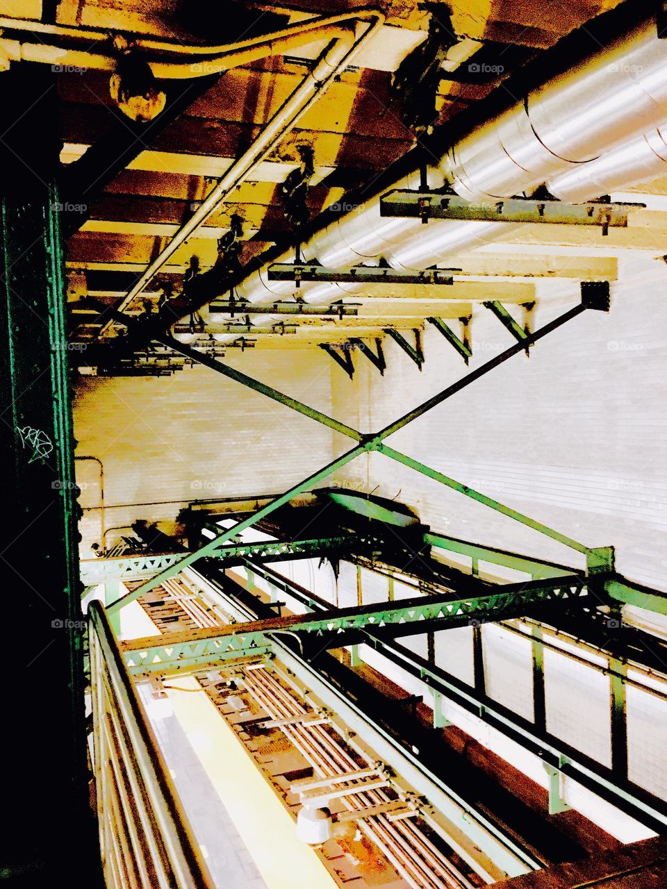 This is a view from underneath of the ceiling of the “Vernon Jackson” 7 train subway station in “Long Island City”, Queens. Ceramic tiles can be seen on the wall in the back, piping and metallic green details above. 2020. Hypnotic Productions