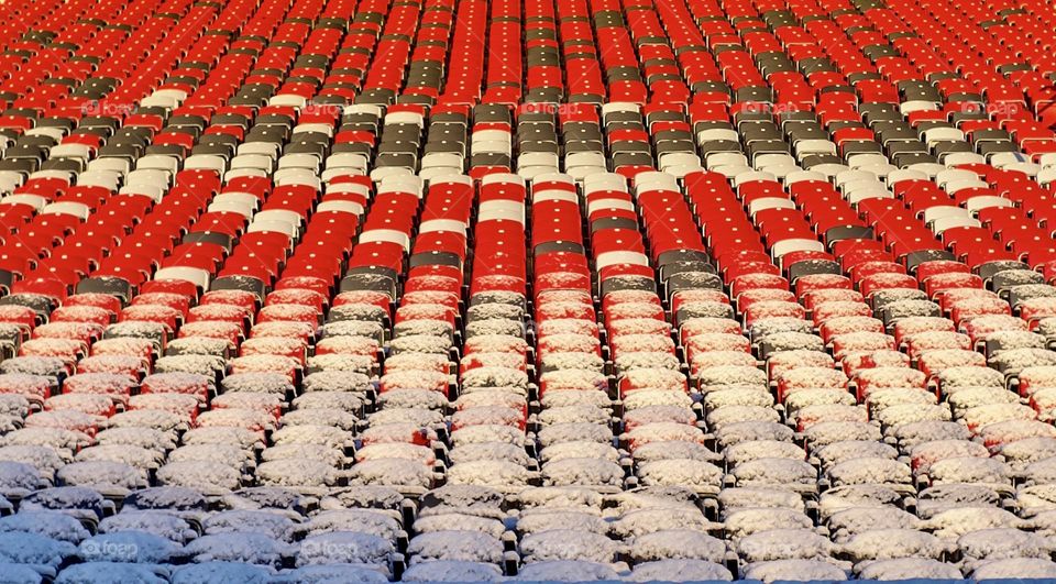 Red and black stadium seats partly covered with snow.