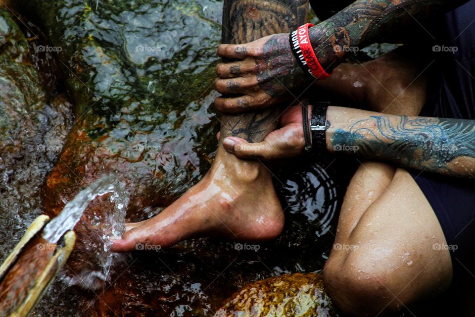 portrait of a person's feet sitting on a river rock with many tattoos on his feet.