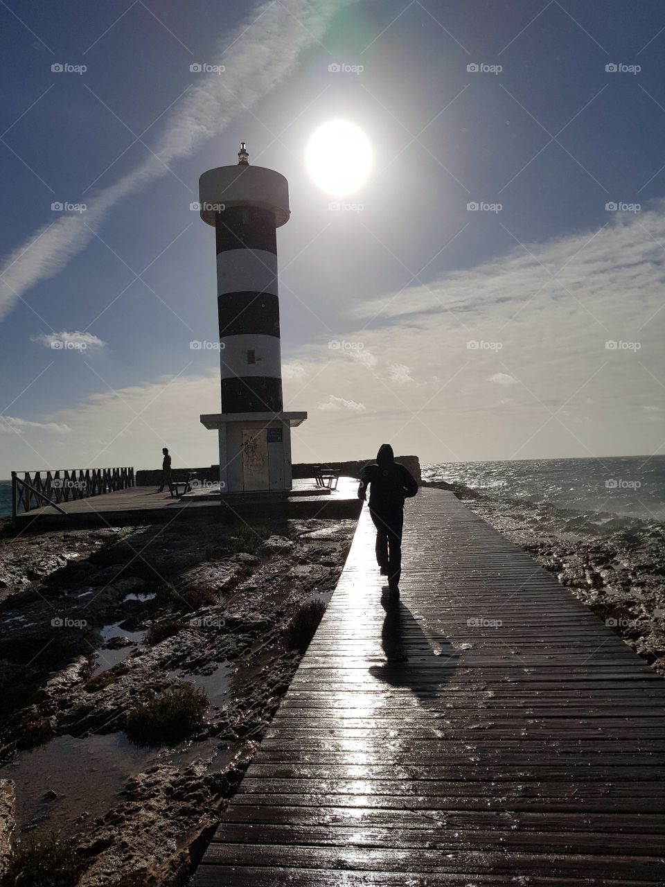 ein Mann der auf einem nassen Steg rennt mit einem Leuchtturm im Hintergrund auf Mallorca