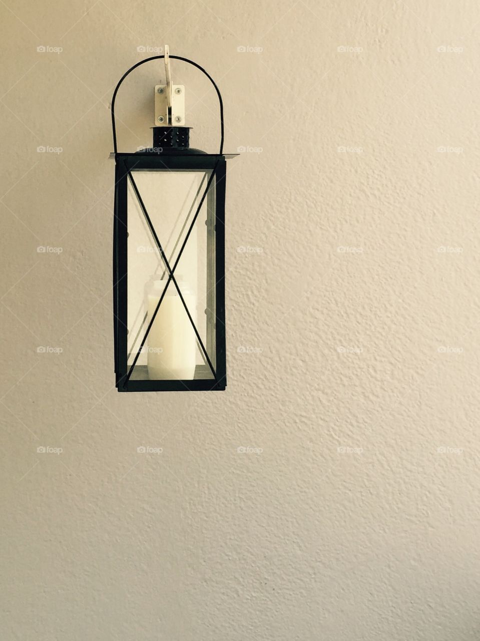 Lantern on the wall. Simple metal candle lantern on the light wall background