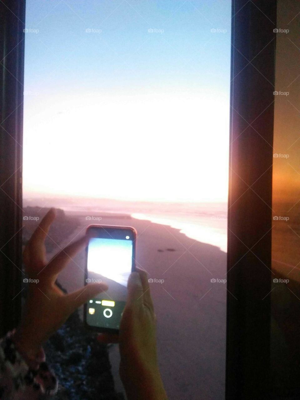 Hands capting the beach from window.